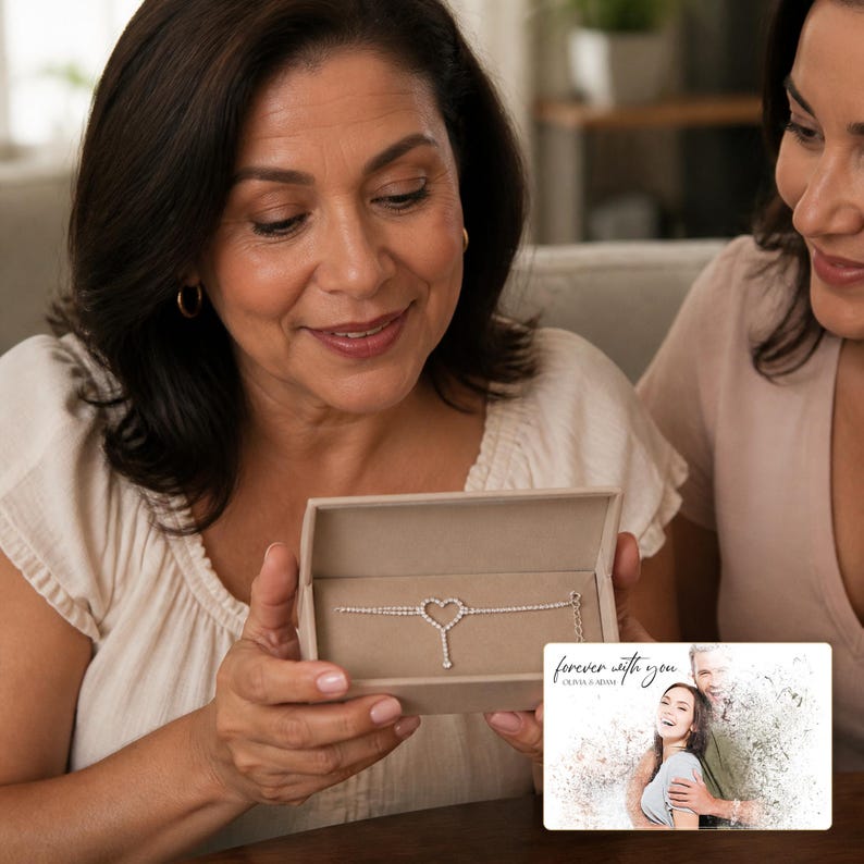 May include: A silver-toned bracelet featuring a central heart-shaped charm with embedded clear stones, presented in a beige rectangular box. Beside the box is a rectangular card displaying a photo of a couple and the text "forever with you OLIVIA & ADAM".