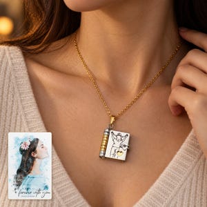 Opening book pendant necklace in the Parent and Child design worn with a cream top, beside a personalized digital greeting card.