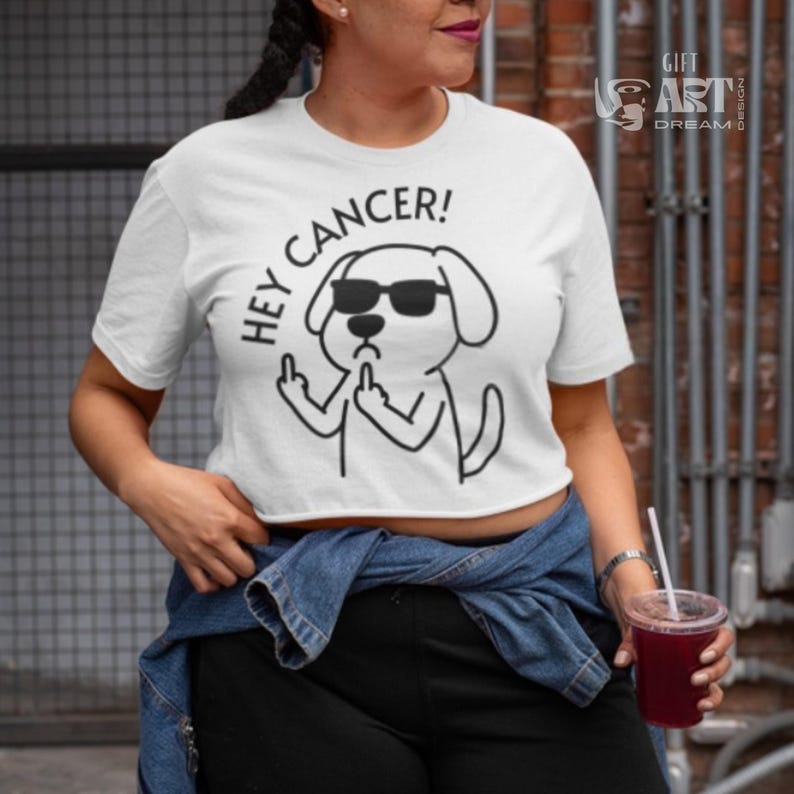 May include: White crop top with a black and white illustration of a dog wearing sunglasses and giving the middle finger. The text "Hey Cancer!" is written above the dog.