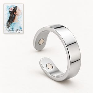 Close detail of the reflective silver-tone ring band and one flush round insert on its inner tip. A personalized digital greeting card is shown alongside.