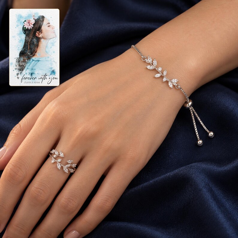 Adult woman's hand wearing both silver-tone botanical pieces against navy evening clothing. A personalized digital greeting card is shown alongside.
