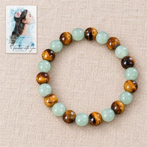 Forest Amber Bead Bracelet arranged on soft ivory linen in a refined neutral flat lay. A personalized digital greeting card is shown alongside.