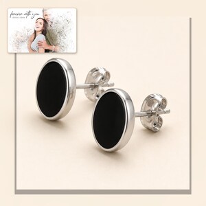 Black oval stud earrings with silver-tone edges, framed product view. A personalized greeting-card example appears in the corner.