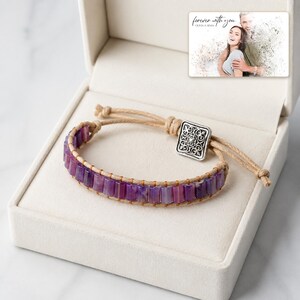 Purple rectangular-bead cord bracelet with a square decorative detail, presentation in an open jewelry box. A personalized greeting-card example appears in the corner.