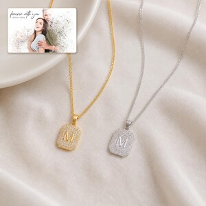 May include: Two necklaces with rectangular pendants featuring the letter M, one in gold and one in silver, both encrusted with small clear stones. An inset image shows a couple with the text forever with you OLIVIA & ADAM.