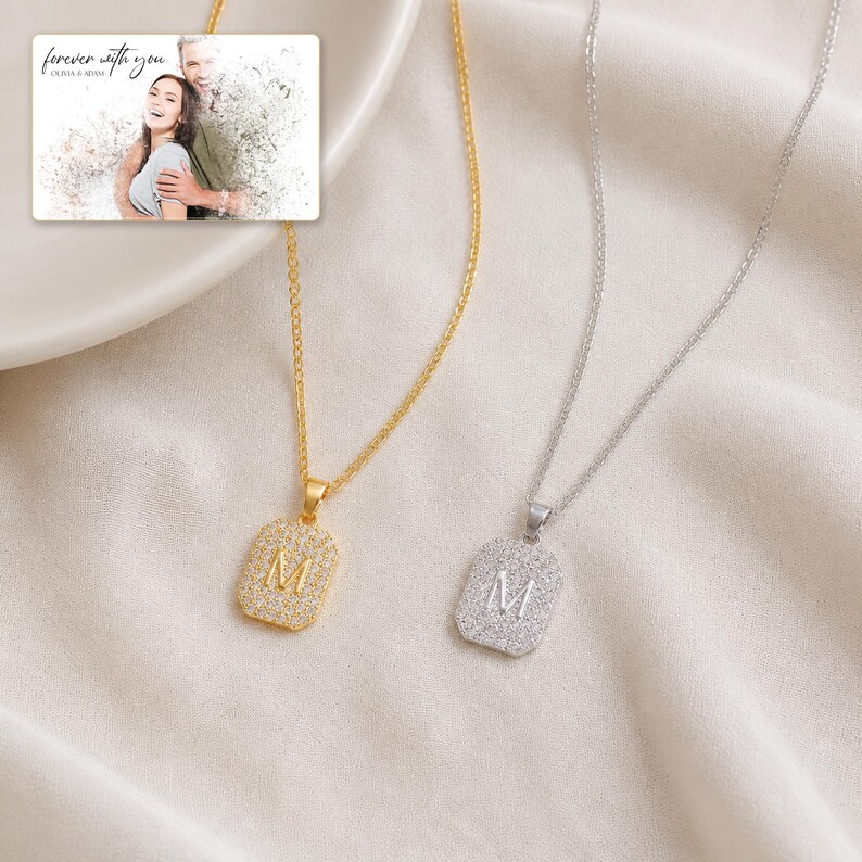 May include: Two necklaces with rectangular pendants featuring the letter M, one in gold and one in silver, both encrusted with small clear stones. An inset image shows a couple with the text forever with you OLIVIA & ADAM.
