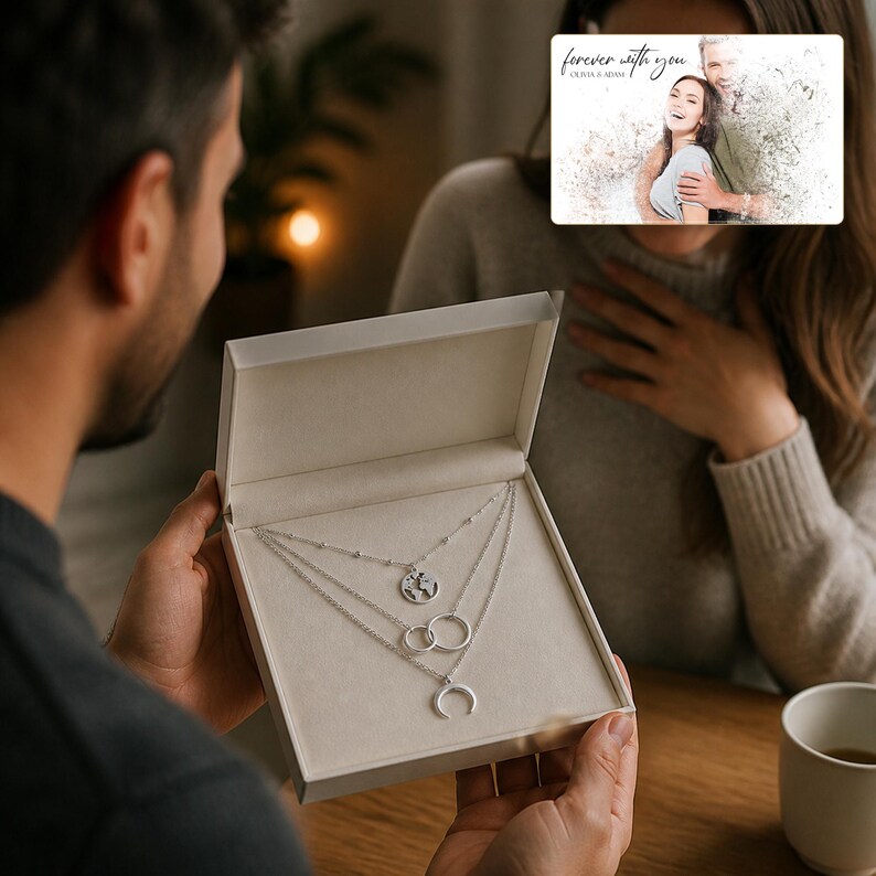 May include: A silver-toned layered necklace set presented in a light-coloured gift box. The set features three distinct chains: one with a small globe pendant, one with two interlocking rings, and one with a crescent moon charm. The box is open.