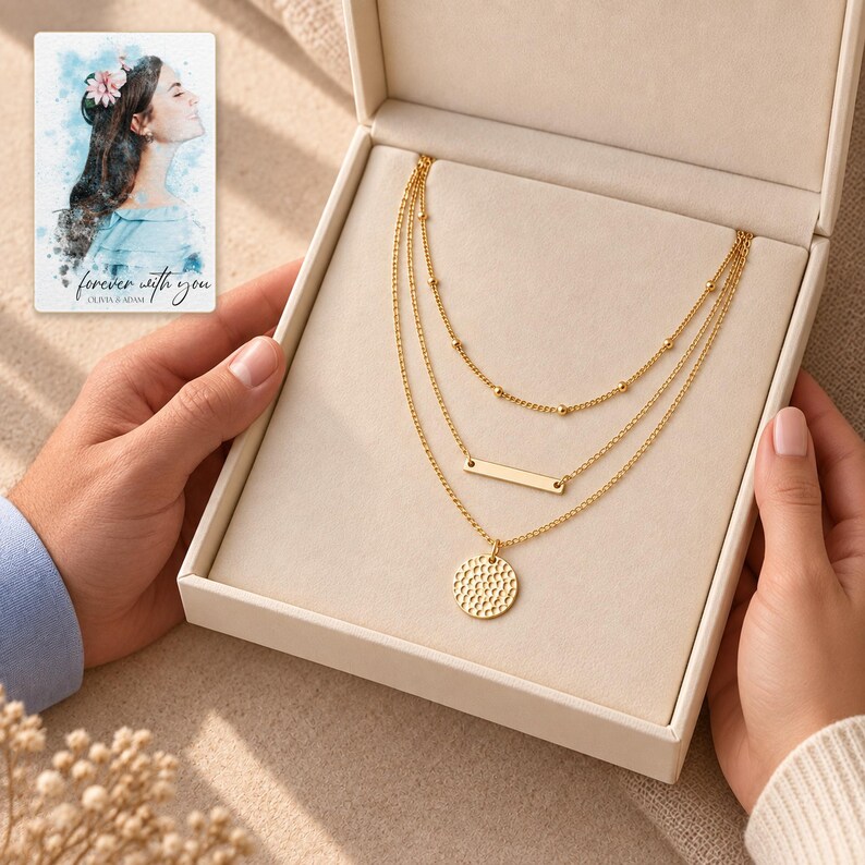 Two adults exchanging an open presentation box containing the satellite, bar and hammered coin necklace. A personalized digital greeting card is shown alongside.