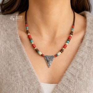 Flatlay lifestyle photo of multicolor beaded silver tone triangle pendant necklace styled on linen and natural stone