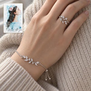 Adult woman's hand wearing the silver-tone leaf bracelet and matching double-vine ring with an oatmeal knit sleeve. A personalized digital greeting card is shown alongside.