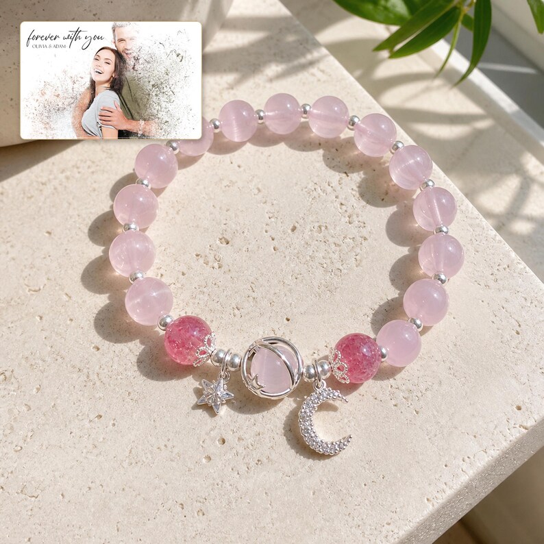 Puede incluir: Una pulsera de cuentas con esferas de cuarzo rosa claro, dos cuentas craqueladas de color rosa oscuro y espaciadores plateados. La pulsera incluye una cuenta central de cuarzo rosa en una jaula plateada, un dije de estrella y uno de luna creciente. Una tarjeta dice forever with you.