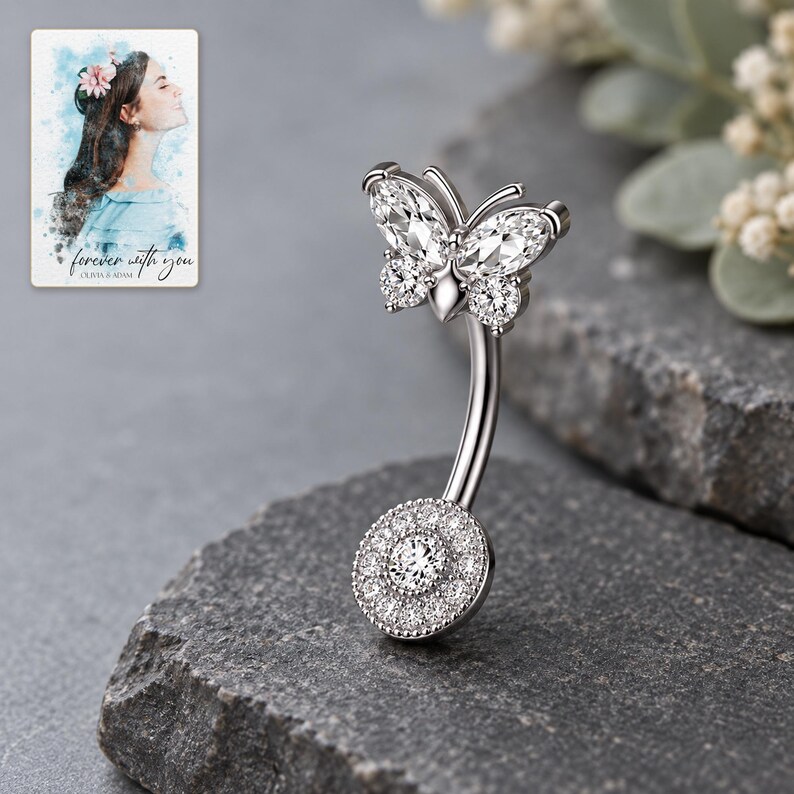 Side view of the butterfly navel bar on matte graphite, showing the curved shaft and setting depth. A personalized digital greeting card is shown alongside.
