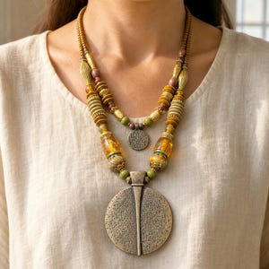 Two-tier bronze, amber and olive beaded statement necklace with layered round pendants displayed on a jewelry bust with the layered beadwork and pendants visible