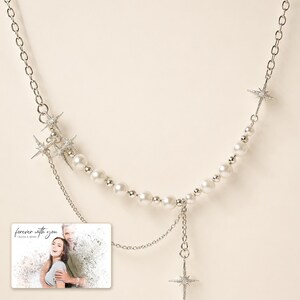 Silver-tone layered necklace with pale beads and pointed star charms, close detail view. A personalized greeting-card example appears in the corner.