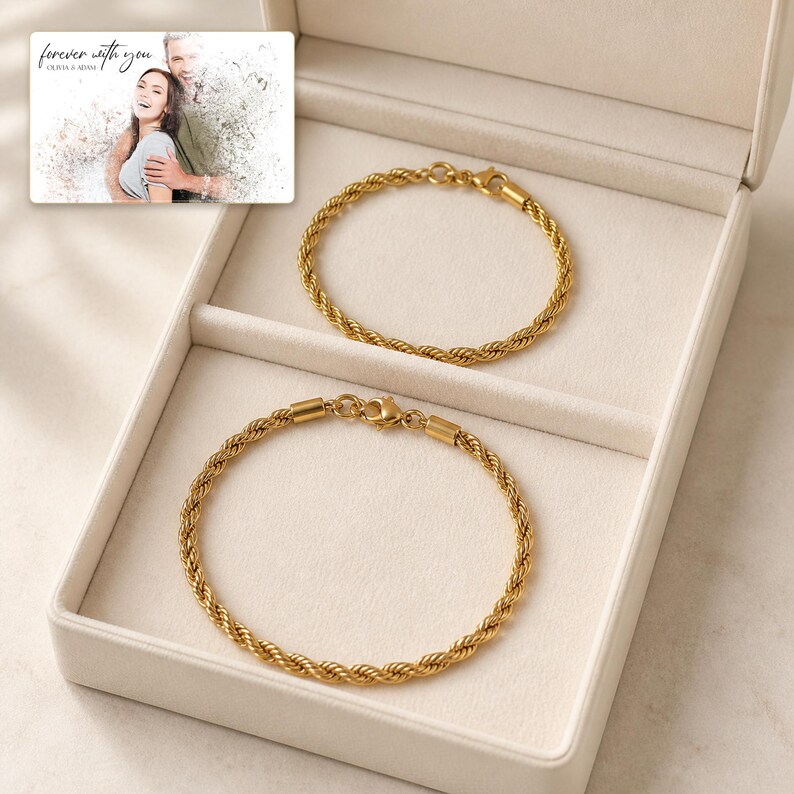 Pu&ograve; includere: Due bracciali a catena ritorta color oro con chiusure a moschettone, presentati in un portagioie beige. &Egrave; incluso un cartoncino rettangolare con una fotografia in bianco e nero di una coppia e il testo "forever with you OLIVIA & ADAM".
