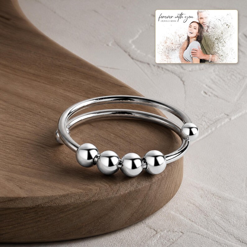 May include: A silver-toned metal ring featuring a double band design with four smooth, round beads that slide along the wire. In the upper right corner, a rectangular card displays a photograph of a couple with the text "forever with you".
