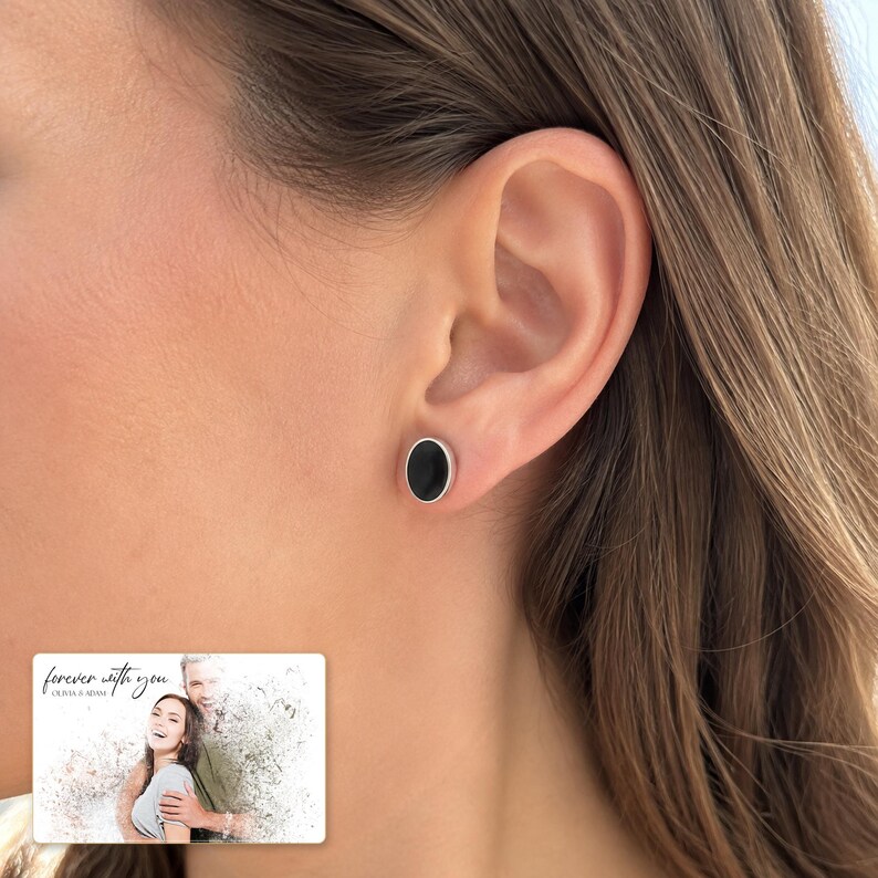 Black oval stud earrings with silver-tone edges, worn view. A personalized greeting-card example appears in the corner.