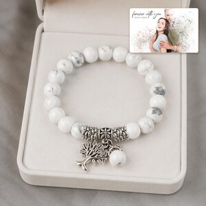 White and gray bead bracelet with silver-tone tree and hanging bead details, presentation in an open jewelry box. A personalized greeting-card example appears in the corner.