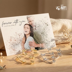 May include: A pair of butterfly ear cuffs, one gold and one silver, sit in front of a card with the words "forever with you" and a photo of a couple. The ear cuffs feature butterfly designs and sparkling details.