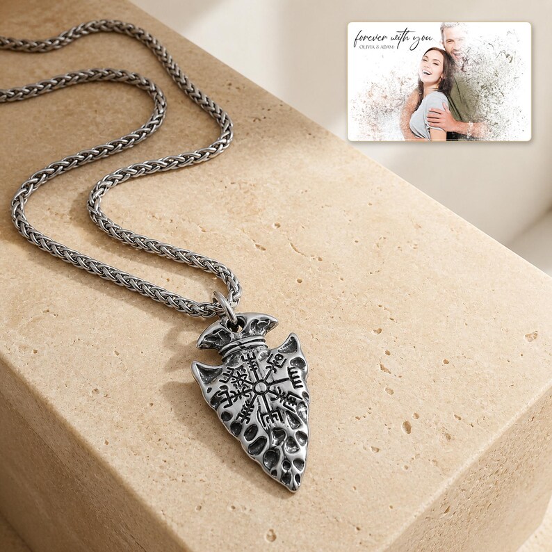 May include: A silver-toned arrowhead pendant necklace featuring an engraved Vegvisir symbol on a wheat chain. Included is a rectangular card displaying a photograph of a couple with the text "forever with you" and "OLIVIA & ADAM" printed on it.