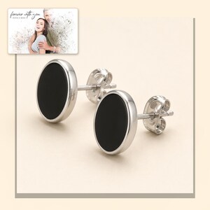 Black oval stud earrings with silver-tone edges, light-bordered product view. A personalized greeting-card example appears in the corner.