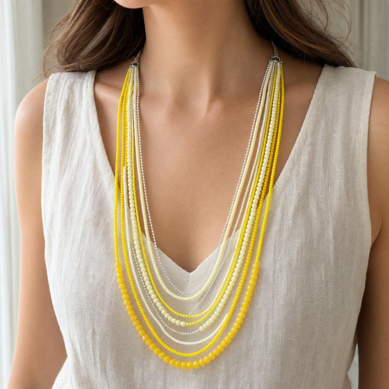 May include: A multi-strand layered necklace featuring alternating strands of small yellow and white beads. The necklace consists of several delicate chains of varying lengths that drape down the chest, creating a cascading effect of bright yellow and soft white tones.