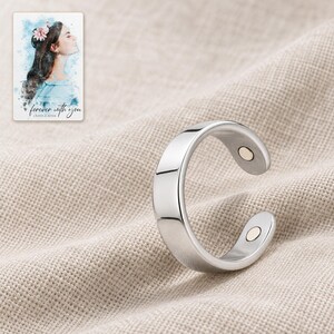 Polished open silver-tone ring resting on folded oatmeal linen with its two inner-tip details facing the camera. A personalized digital greeting card is shown alongside.