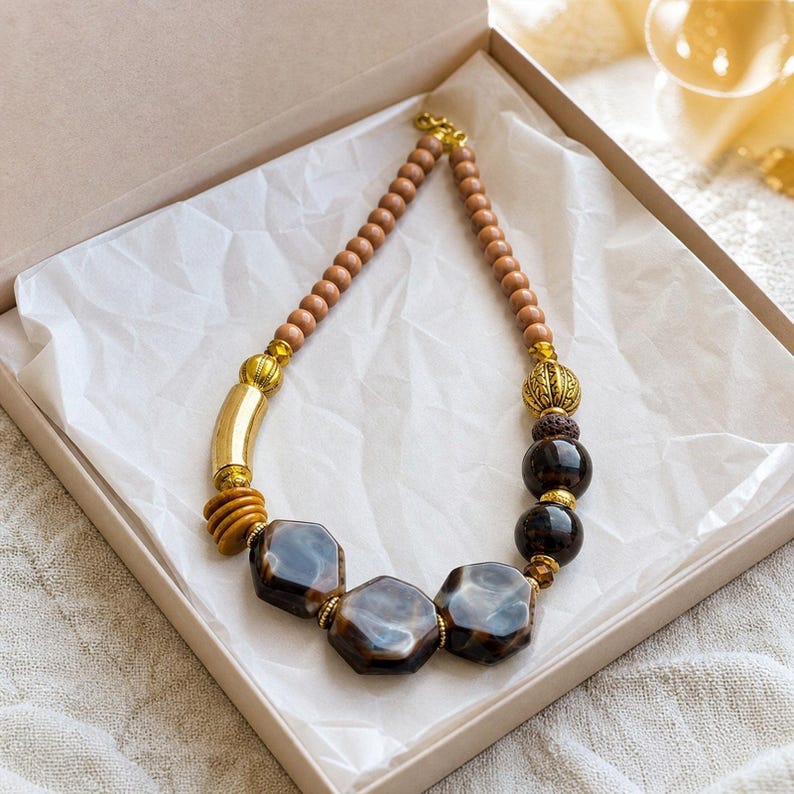 May include: A necklace featuring a strand of small light brown wooden beads, accented with gold-toned metal cylinders and spheres, dark brown round beads, and three large, polished, hexagonal dark brown marbled resin focal beads.