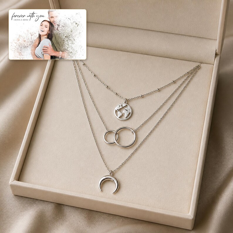 May include: A silver-toned layered necklace set featuring three distinct chains. The top chain has a globe pendant, the middle chain displays two interlocking circles, and the bottom chain holds a crescent moon charm. A photo card reads "forever with you".