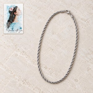 Full silver-tone twisted rope necklace arranged in a close oval on pale stone style with its lobster clasp visible. A personalized digital greeting card is shown alongside.