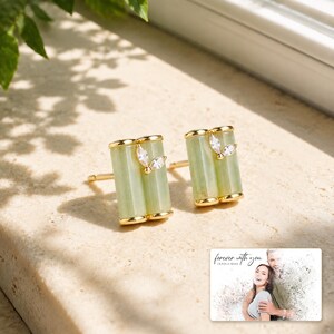 Pale green bamboo-shaped stud earrings with gold-tone edges, light-bordered product view. A personalized greeting-card example appears in the corner.
