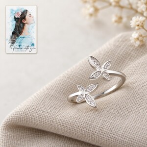 Silver-tone double butterfly open ring on softly folded oatmeal linen. A personalized digital greeting card is shown alongside.