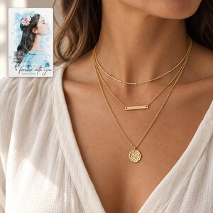 Adult woman wearing the satellite, slim bar and hammered coin necklace with an ivory blouse. A personalized digital greeting card is shown alongside.