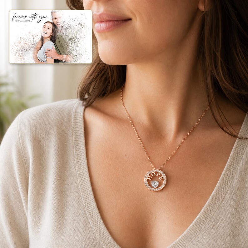Puede incluir: Un collar con colgante circular en tono oro rosa que presenta la palabra HOPE en letras may&uacute;sculas y una peque&ntilde;a piedra transparente en forma de coraz&oacute;n en el centro. El colgante cuelga de una cadena fina. Un recuadro muestra una foto con el texto forever with you.