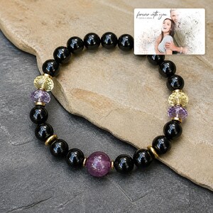 May include: A beaded bracelet featuring smooth black round beads, faceted purple beads, and faceted yellow beads, accented with small gold-toned metal spacers. A small rectangular card is included with the text "forever with you" and "OLIVIA & ADAM" above a photograph of a couple.