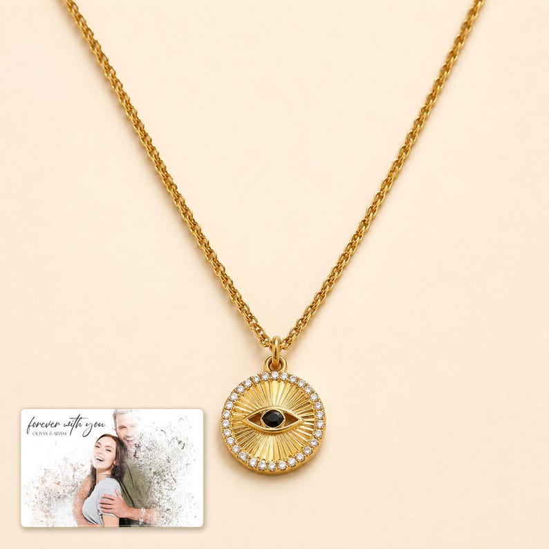 Gold-tone necklace with a round sunburst and black eye detail, display view. A personalized greeting-card example appears in the corner.