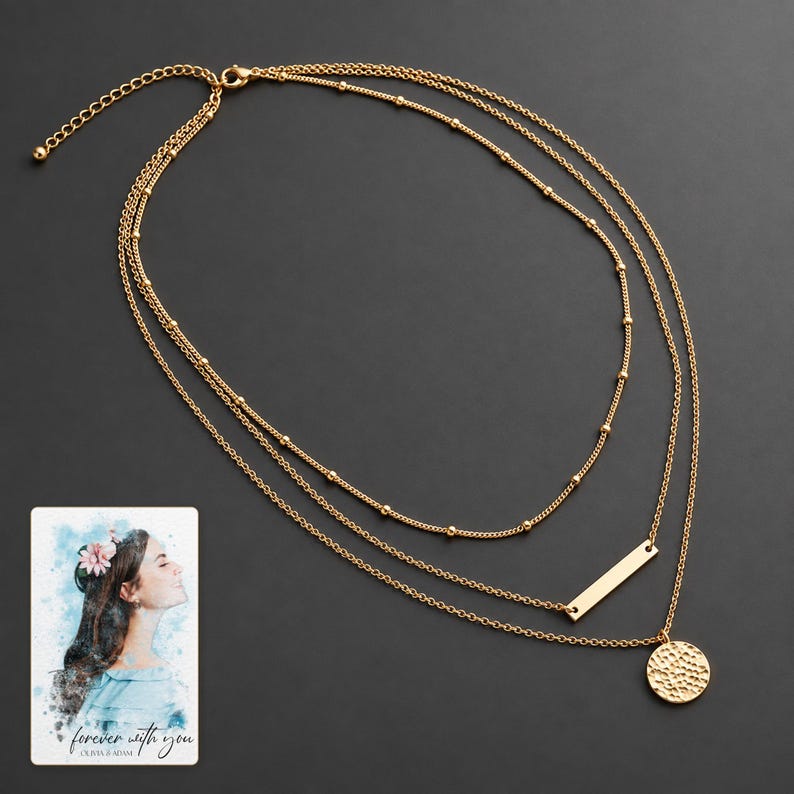 Gold-tone satellite, bar and hammered coin necklace laid against matte graphite, with all chains visible. A personalized digital greeting card is shown alongside.