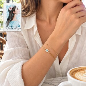 Gold Tone Evil Eye Bracelet Duo worn by an adult in a natural daytime lifestyle scene. A personalized digital greeting card is shown alongside.