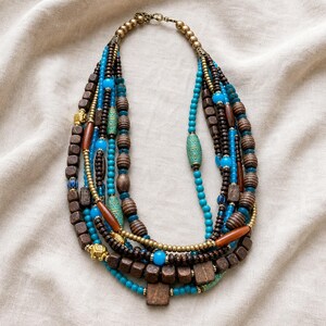 Gift ready presentation of Turquoise blue and dark brown multistrand statement beaded necklace with antique brass accents in an open jewelry box lined with natural ivory linen