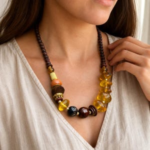 Asymmetric honey amber and dark brown single strand statement beaded necklace displayed on a jewelry bust with its amber pebble and dark wood bead sequence visible