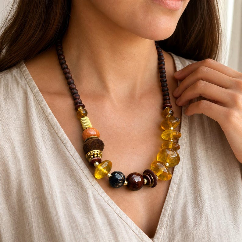 Asymmetric honey amber and dark brown single strand statement beaded necklace displayed on a jewelry bust with its amber pebble and dark wood bead sequence visible