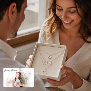 May include: A silver-toned multi-strand necklace set featuring three distinct pendants: a circular world map charm, two interlocking rings, and a crescent moon shape, presented in a square white gift box with a card reading forever with you.