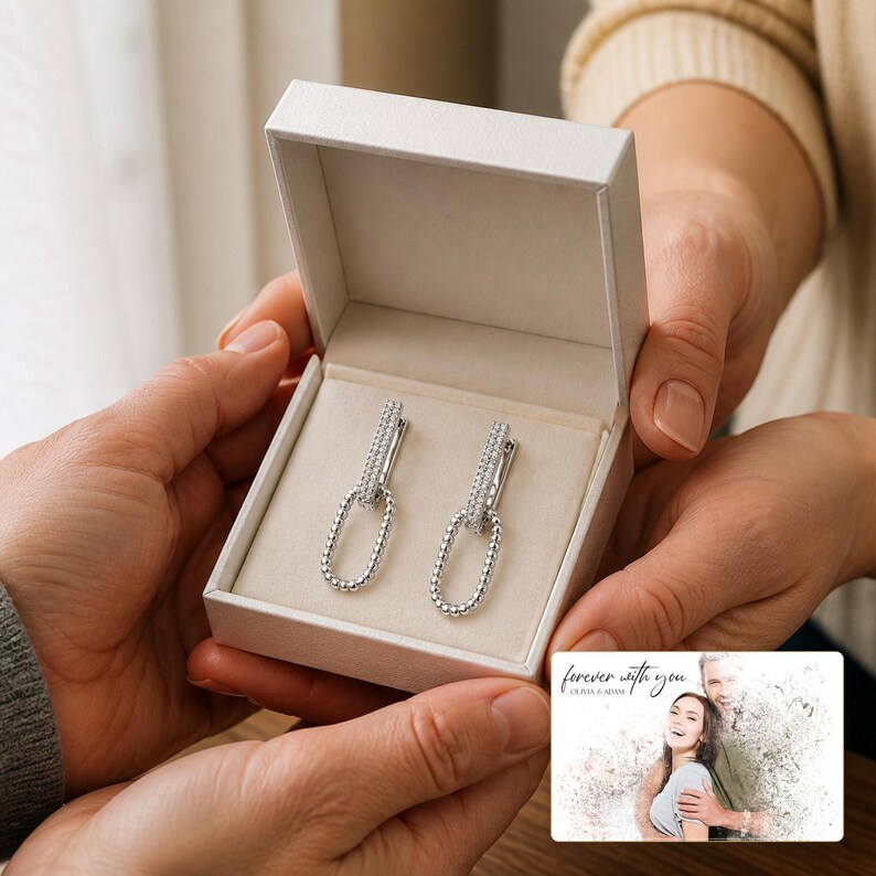 May include: A pair of silver-toned drop earrings featuring a rectangular top bar encrusted with small clear stones and a dangling oval link with a beaded texture, presented in a white jewellery box with a card reading forever with you.