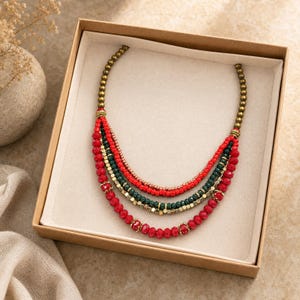 Five strand red deep green copper and antique gold layered beaded statement necklace worn with an ivory linen top in warm natural window light