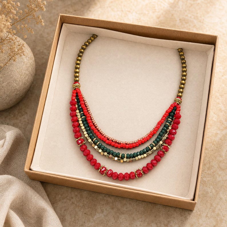 Five strand red deep green copper and antique gold layered beaded statement necklace worn with an ivory linen top in warm natural window light