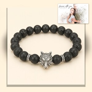 Black bead bracelet with silver-tone wolf-head detail, light-bordered product view. A personalized greeting-card example appears in the corner.