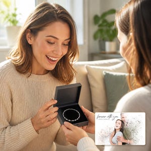 May include: A silver chain bracelet with small round beads inside a dark gray square gift box. Next to the box is a rectangular card featuring a printed photograph of a couple with the text "forever with you" and "OLIVIA & ADAM" in script.