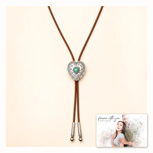 Brown cord bolo necklace with a silver-tone heart slide and turquoise-color center, catalog view. A personalized greeting-card example appears in the corner.