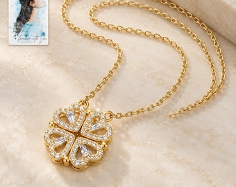 May include: A gold-tone necklace featuring a pendant shaped like a four-leaf clover, adorned with small clear stones and baguette-cut crystals. The pendant is designed to fold into a heart shape. A small card with a watercolor illustration and the text "forever with you" is visible.