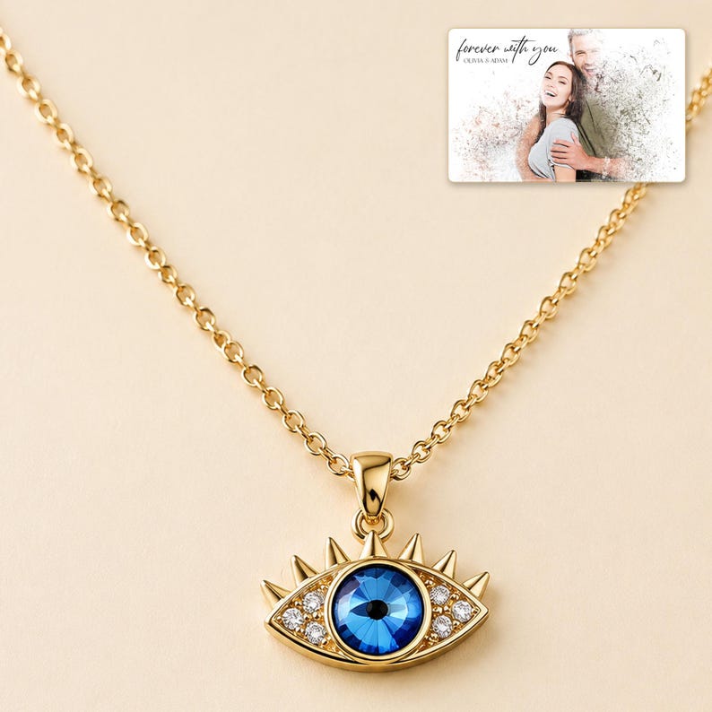 Gold-tone necklace with a blue eye-shaped pendant, close detail view. A personalized greeting-card example appears in the corner.